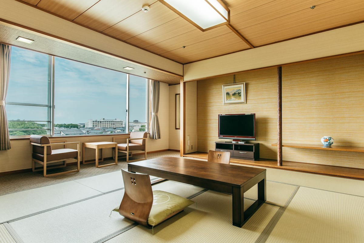 A modern meeting room with a large table, chairs, a television, and a view of the city through large windows.