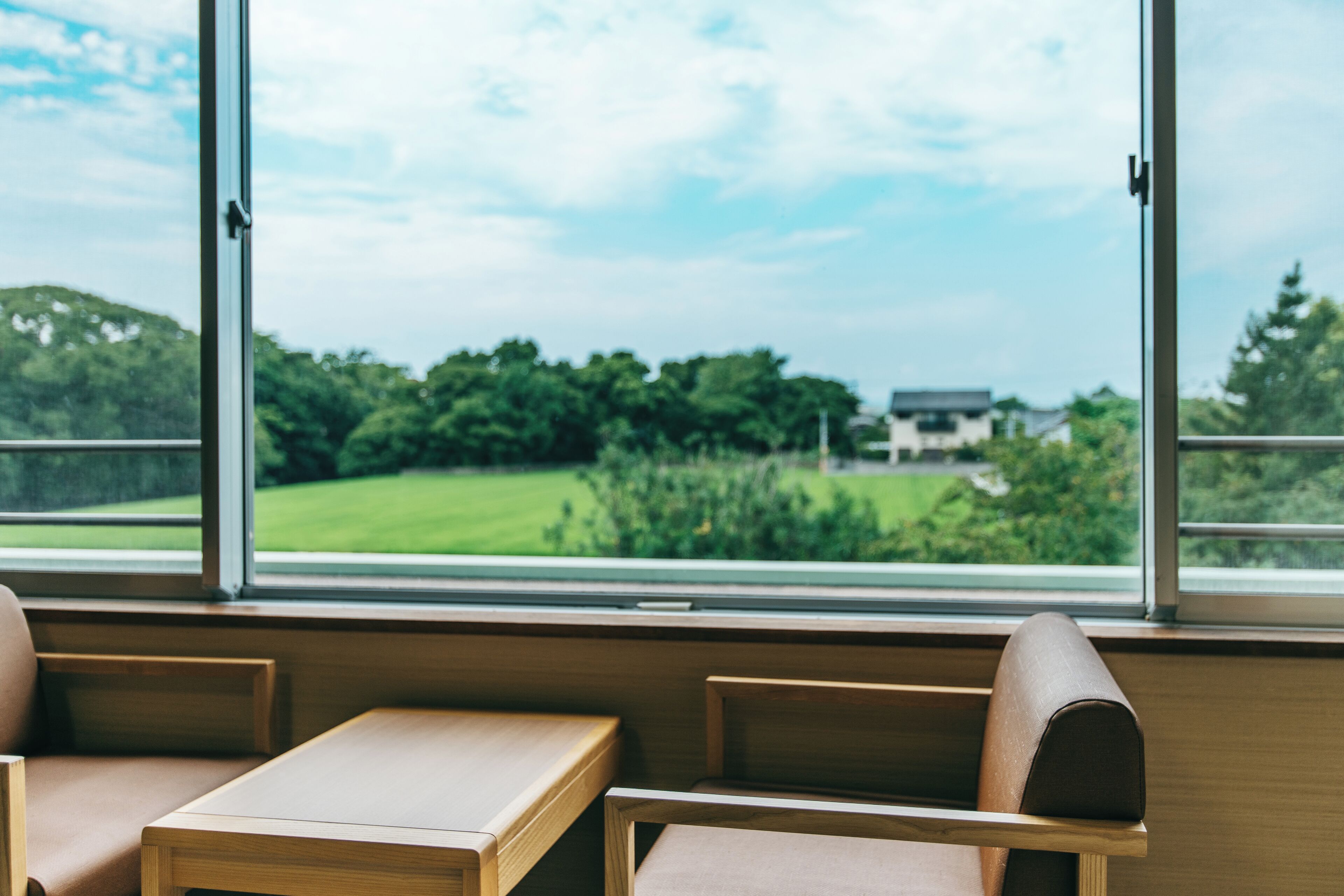 A room with a view of a green landscape through large windows.