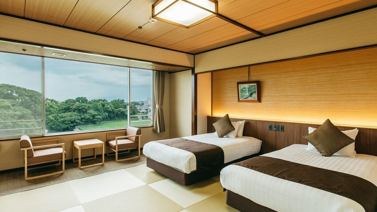 Een hotelkamer met twee bedden, een groot raam, een klein tafeltje en een stoel.