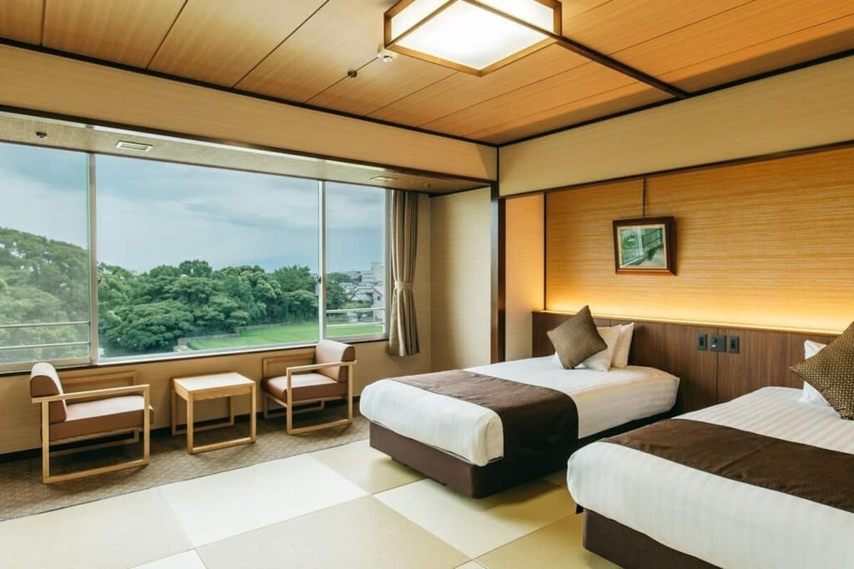 A hotel room with two beds, a large window, a small table, and a chair.