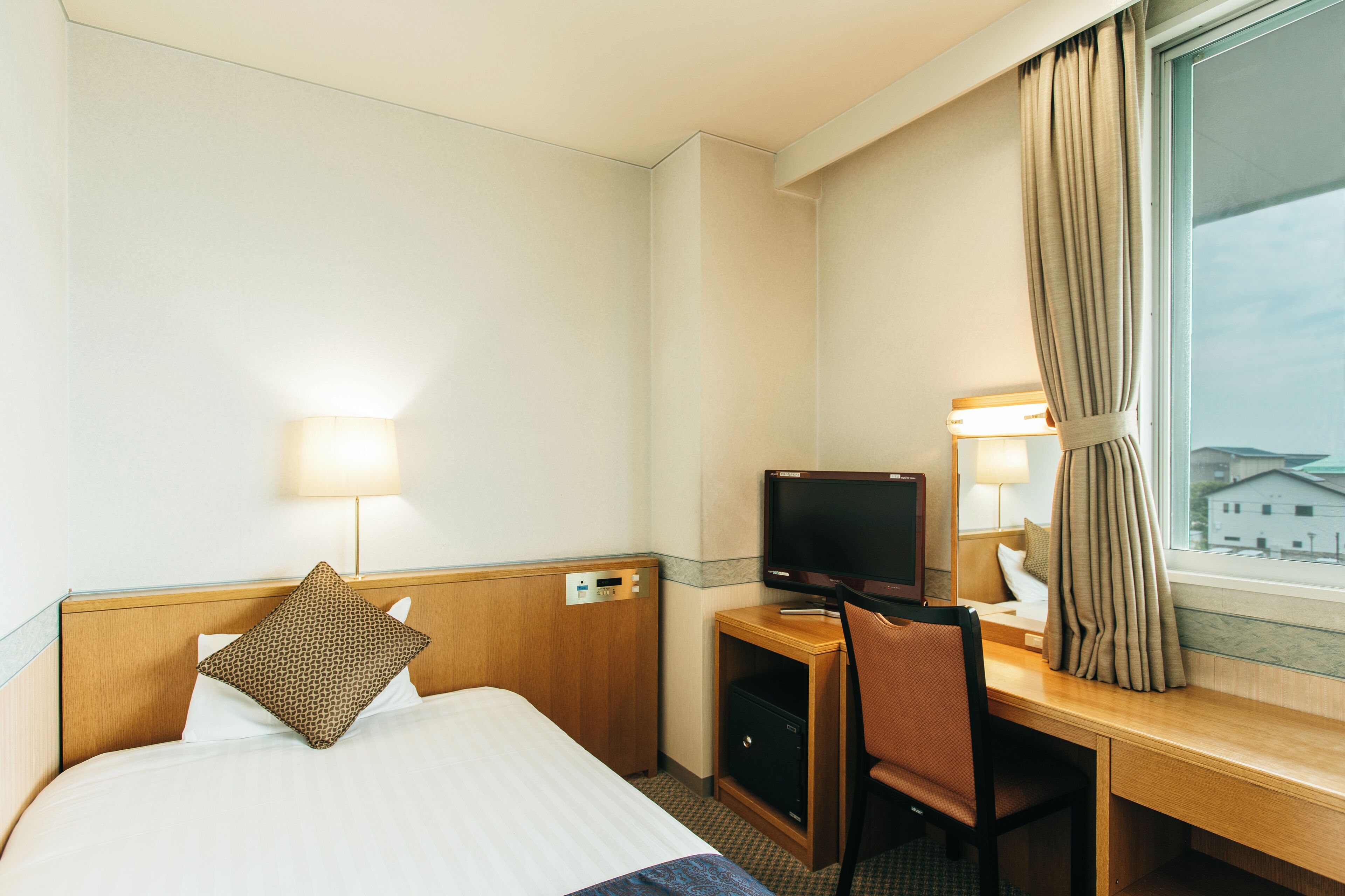 Habitación de hotel con cama, escritorio con computadora, televisor y ventana con cortinas.