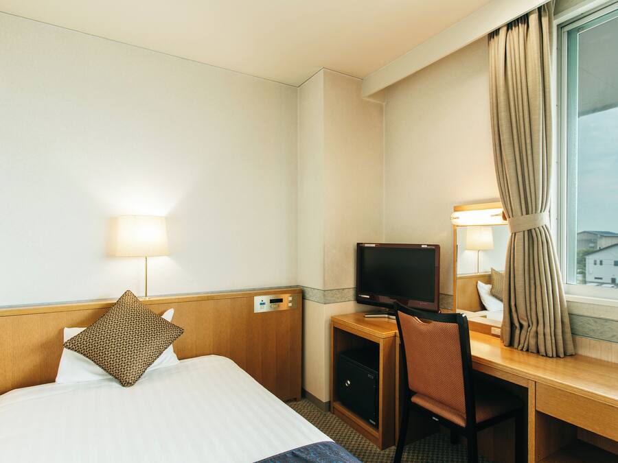 Habitación de hotel con cama, escritorio con computadora, televisor y ventana con cortinas.