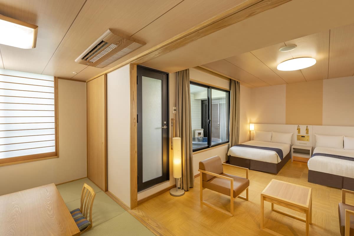 A hotel room with a wooden floor, two beds, a sofa, a table, and a lamp.