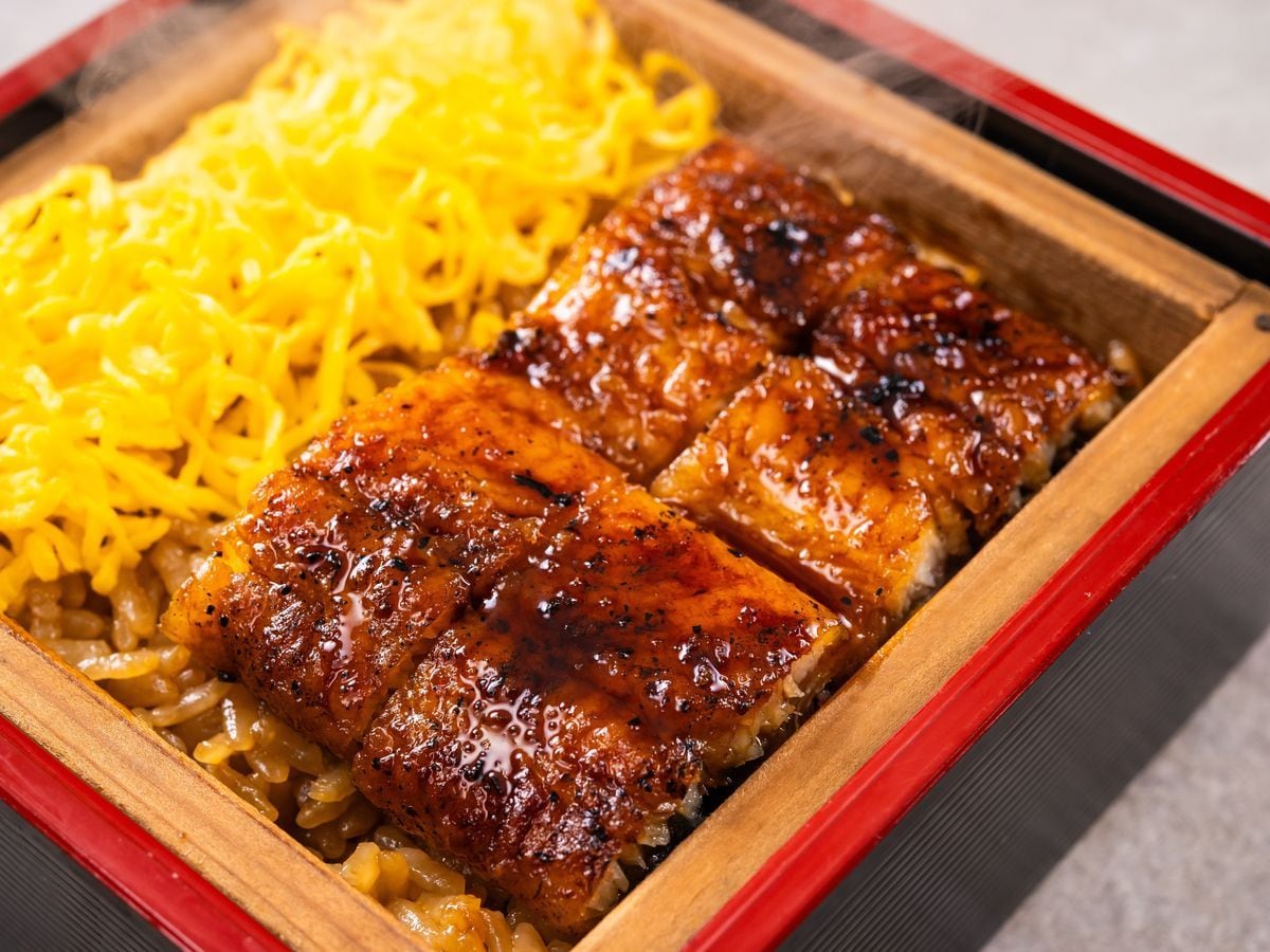 A wooden serving dish with grilled meat and yellow noodles.