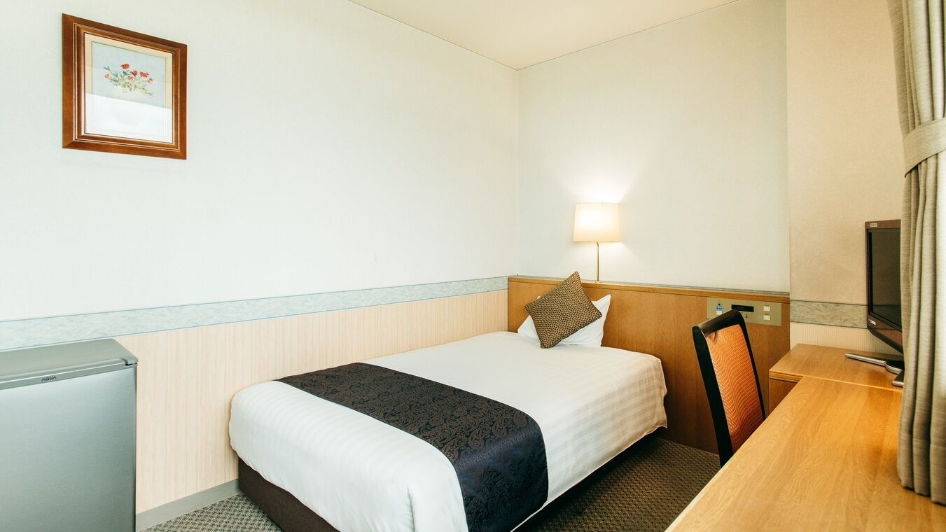 Een hotelkamer met een bed, een bureau, een lamp, een televisie en een ingelijst schilderij aan de muur.