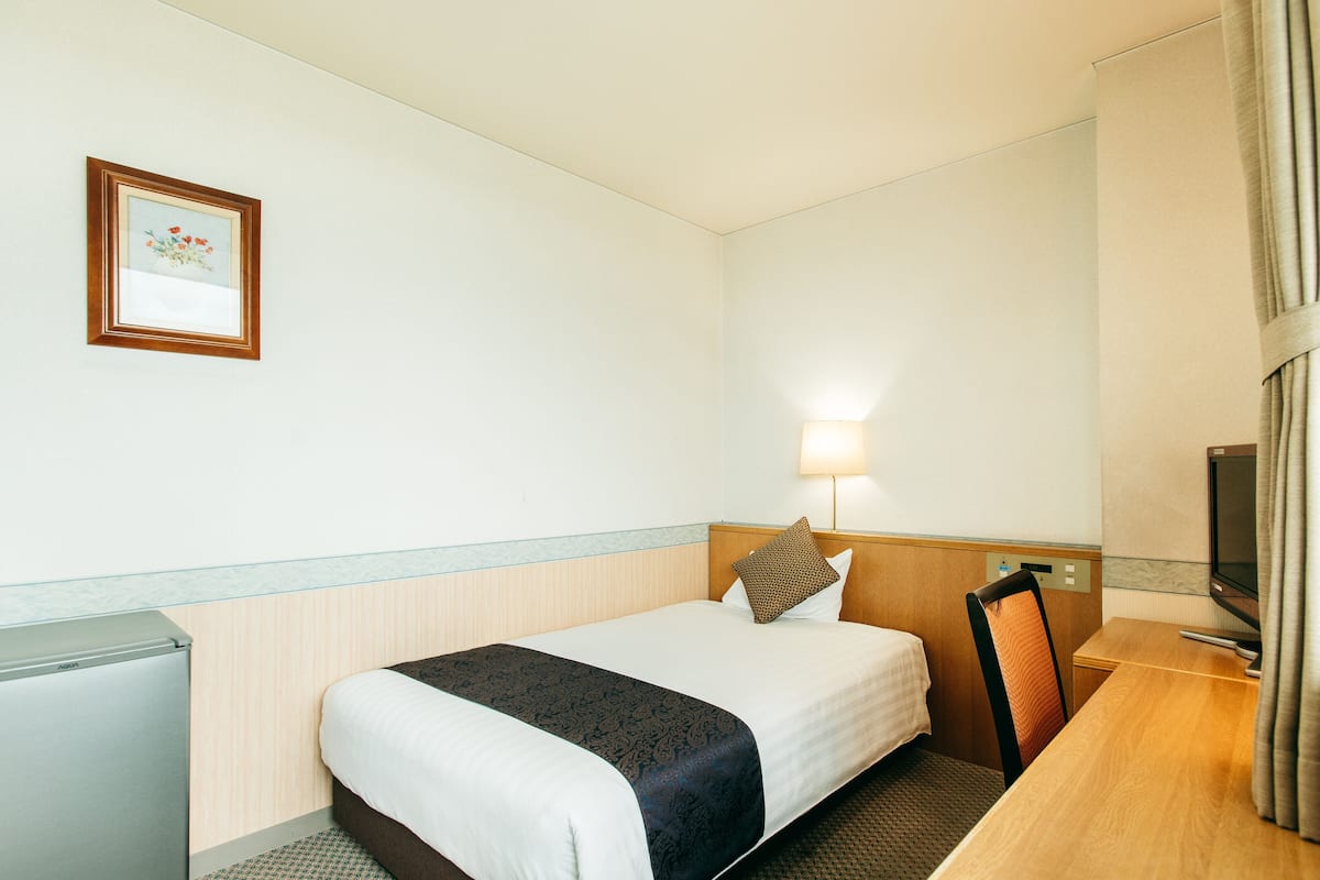 A hotel room with a bed, bedside table, lamp, TV, and a small refrigerator.