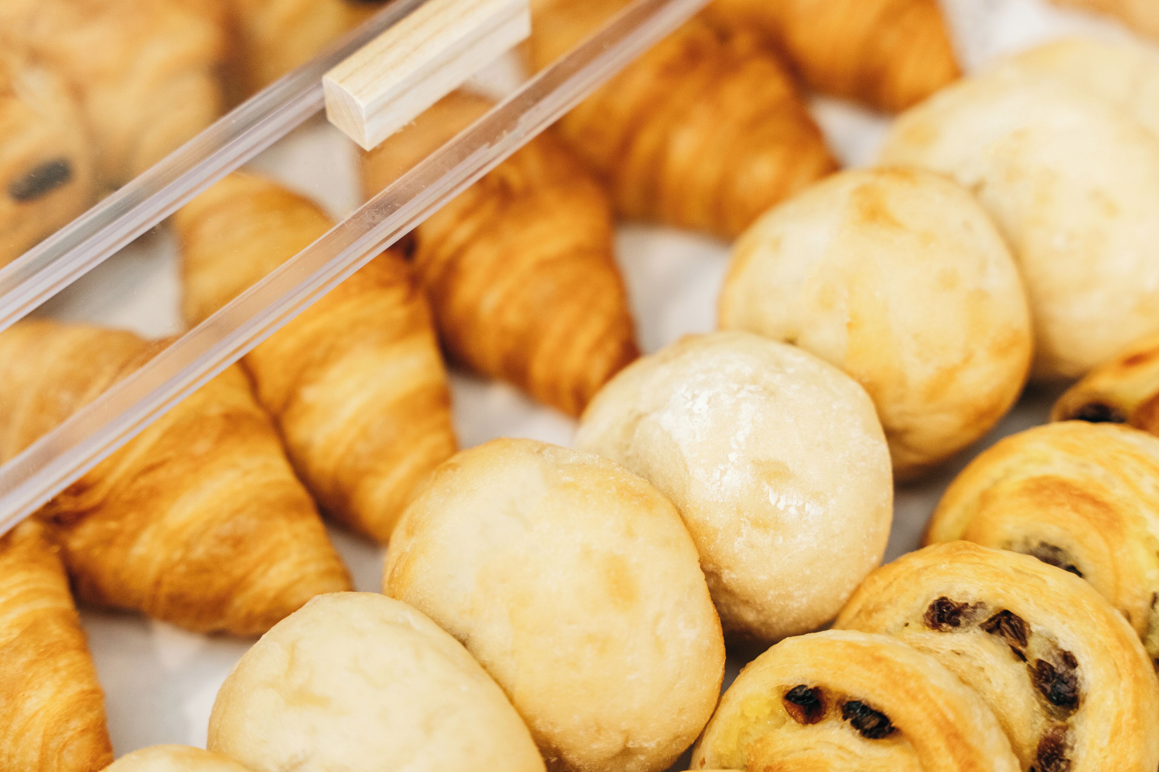 Una variedad de pasteles, incluyendo croissants y panes redondos, expuestos en una panadería.