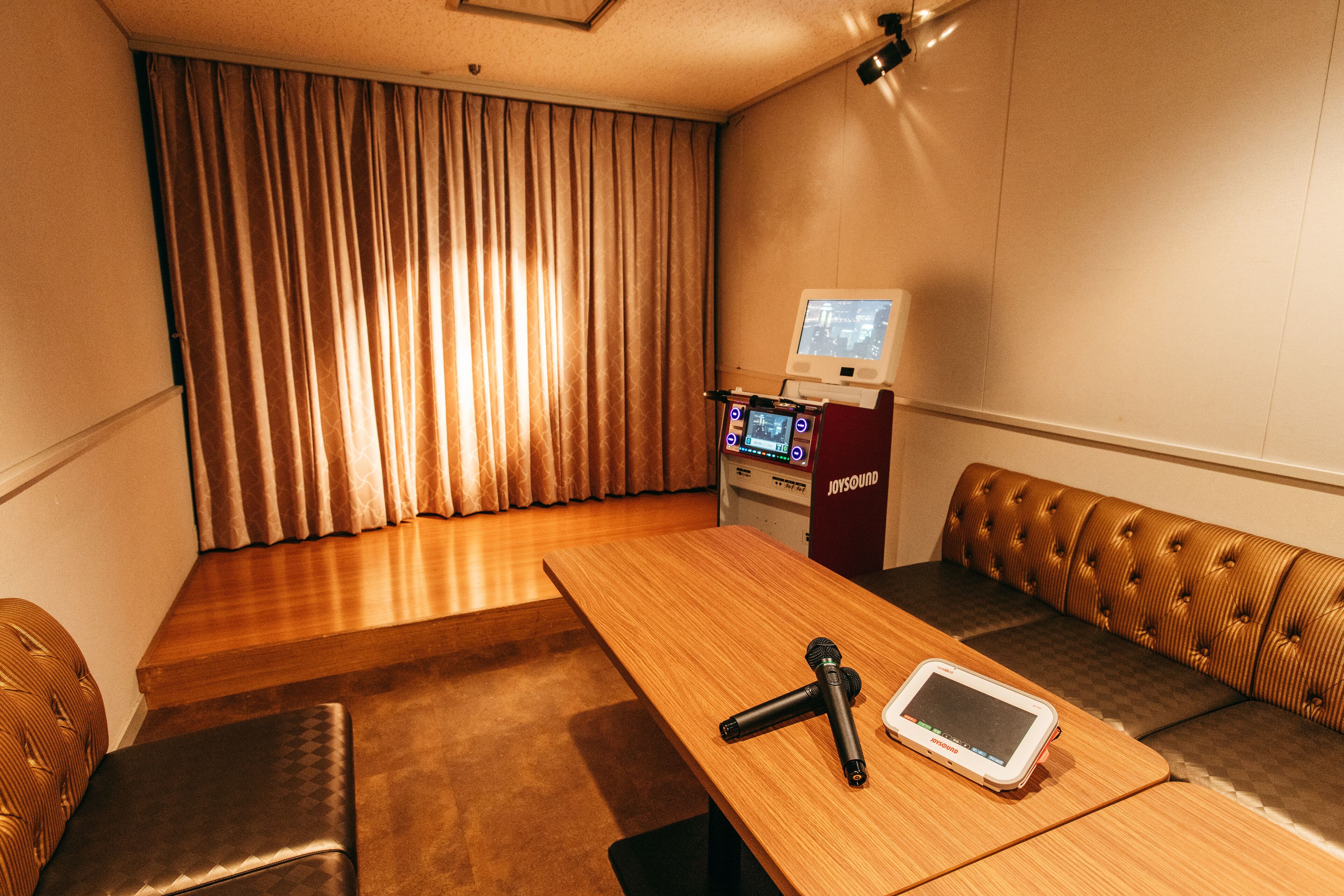 A room with a wooden table, a microphone, a tablet, a sofa, and a jukebox.