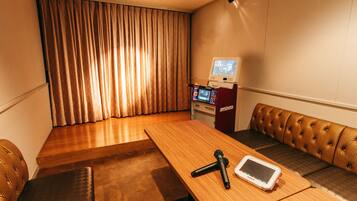 A room with a wooden table, a microphone, a tablet, a sofa, and a jukebox.