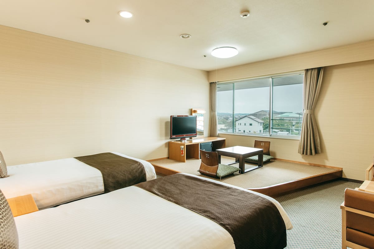 A hotel room with two beds, a desk, a chair, a television, and a window with a view.