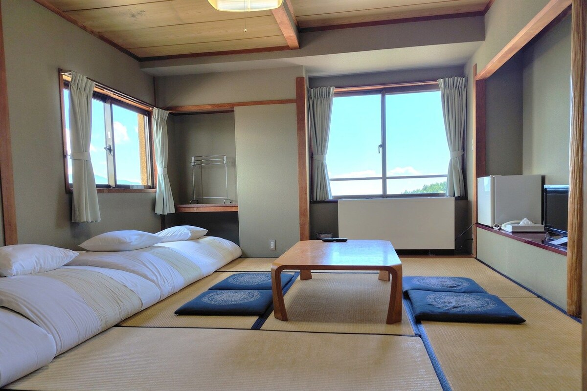 A traditional Japanese-style room with tatami mats, a futon bed, a small wooden table, and a television.