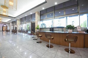 A spacious lobby with a reception desk, several bar stools, and a large window providing natural light.