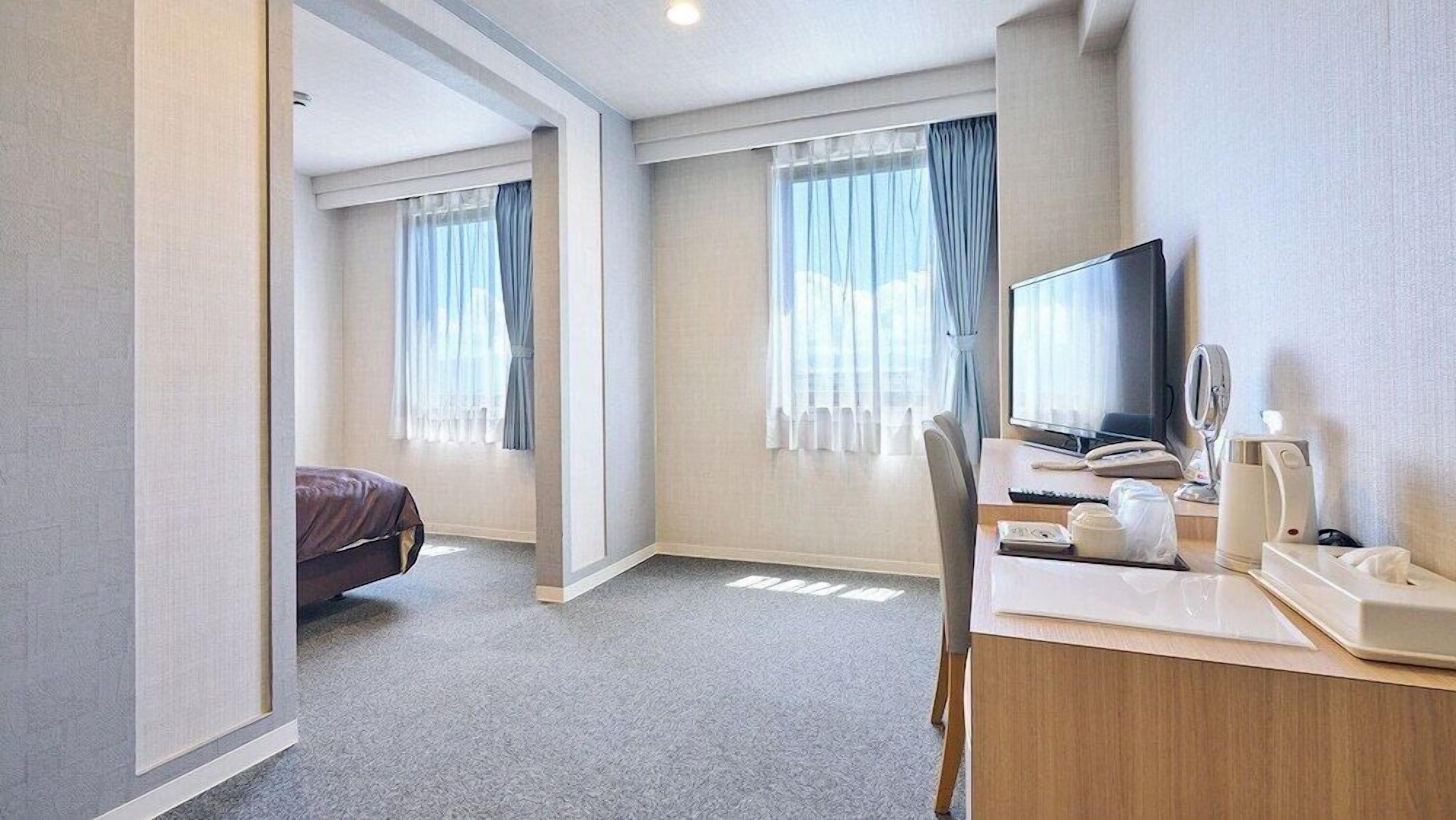 Une chambre d’hôtel avec un lit, un bureau avec une télévision, une chaise et une fenêtre avec des rideaux.