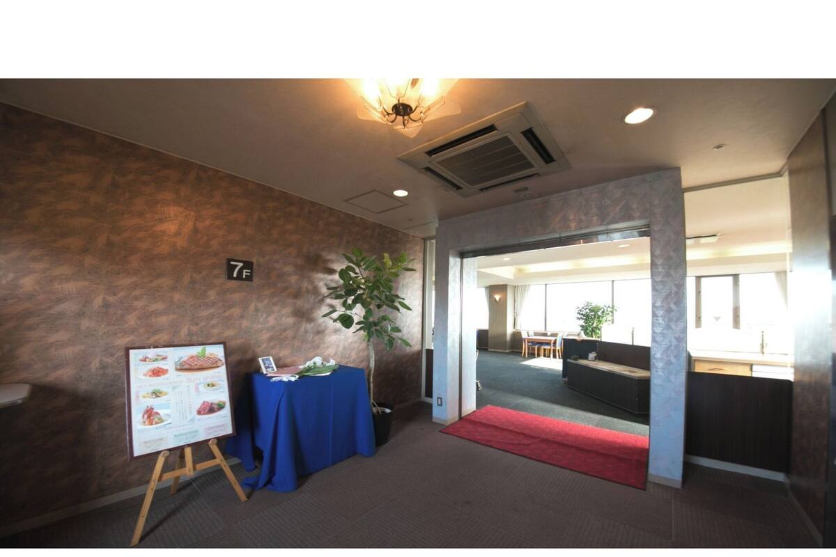 A hotel room with a wooden floor, a red carpet, a table with a blue tablecloth, a plant, and a wall-mounted air conditioning unit.