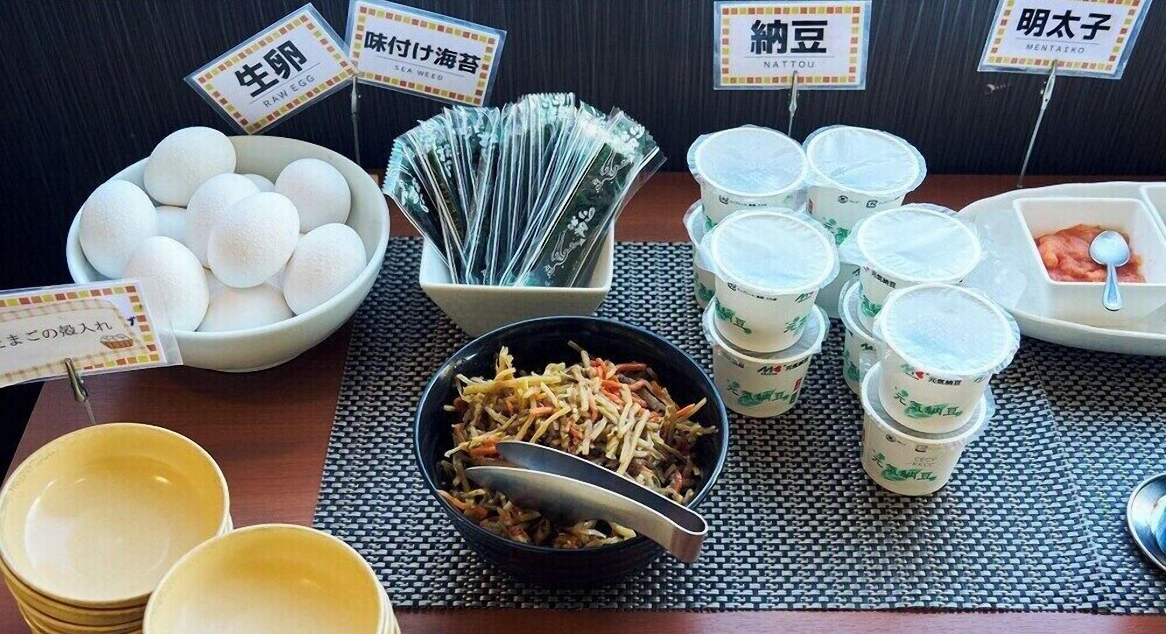 A table with various food items and containers, including a bowl of eggs, a bowl of shredded vegetables, and several cups with lids.