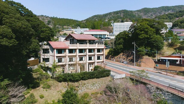 Um edifício de vários andares com telhado vermelho, rodeado por vegetação e colinas.