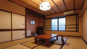 Um quarto japonês tradicional com piso de tatame, uma mesa baixa, uma televisão e portas deslizantes.