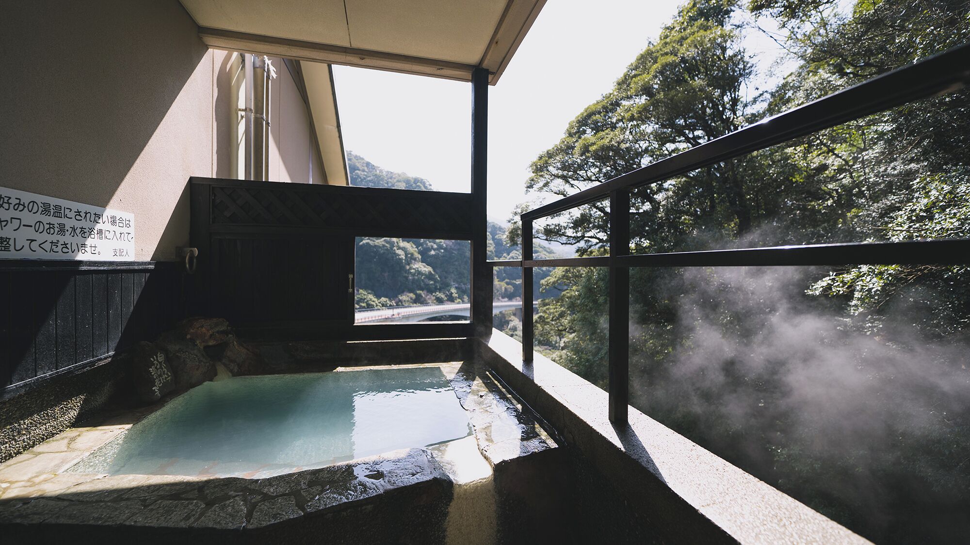 A hot spring bath area with a view of a bridge and forest.