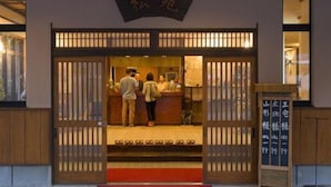 Um edifício japonês tradicional com fachada de madeira, entrada com tapete vermelho e uma placa com caracteres japoneses.