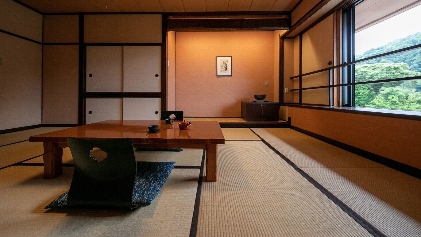 A traditional Japanese room with tatami flooring, a wooden table, and a view of greenery through a window.