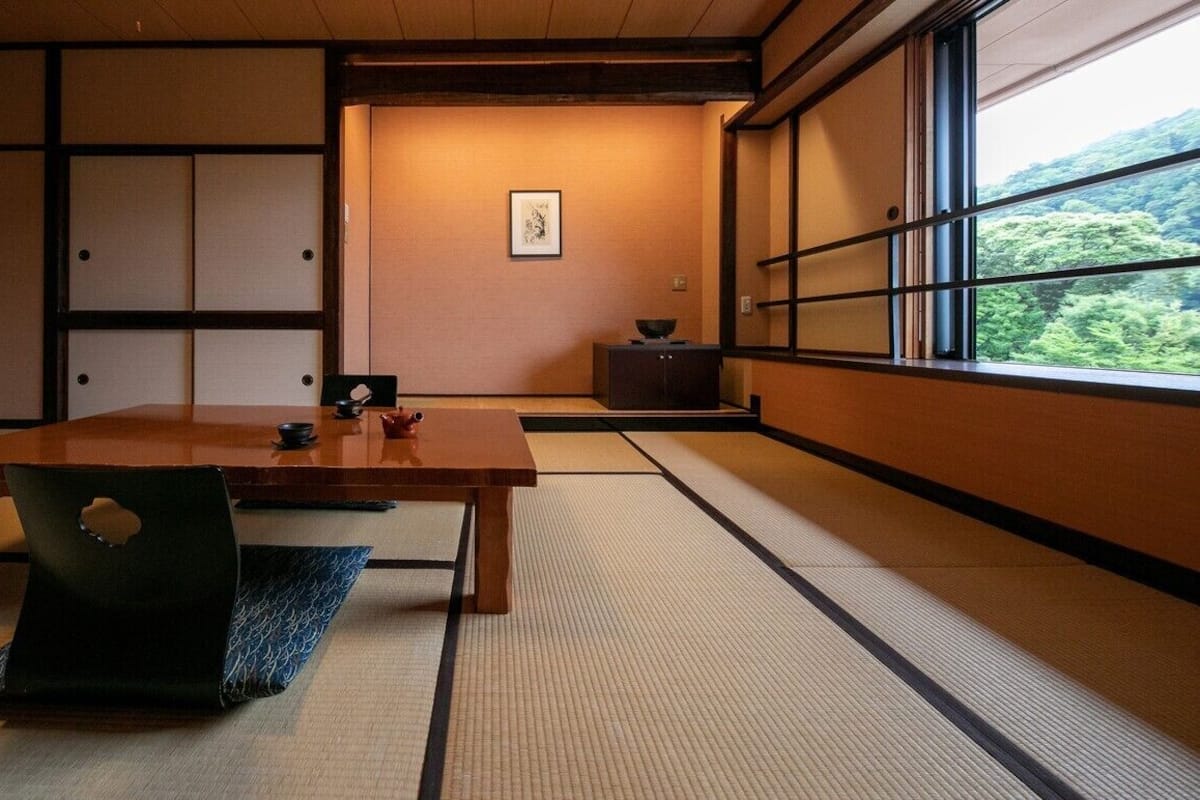 A traditional Japanese room with tatami flooring, a wooden table, and a view of greenery through a window.