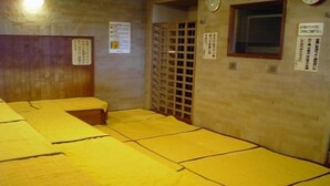 A room with multiple beds covered in yellow sheets, wooden headboards, and a window with a clock. - Hotel Peaceful (Kumamoto)
