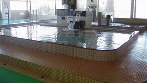 A large indoor swimming pool with a waterfall feature, tiled walls, and large windows. - Hotel Peaceful (Kumamoto)