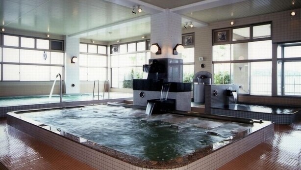 A large indoor swimming pool with a waterfall feature, surrounded by large windows and a tiled floor. - Hotel Peaceful (Kumamoto)
