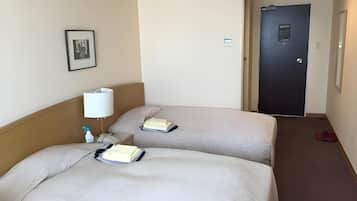 A hotel room with two beds, a bedside table with a lamp, a framed picture on the wall, and a door in the background.