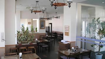 A restaurant interior with multiple dining tables and chairs, ceiling fans, and hanging light fixtures.
