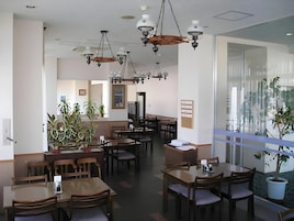 Interior de restaurante con varias mesas y sillas, ventiladores de techo e iluminación colgante.