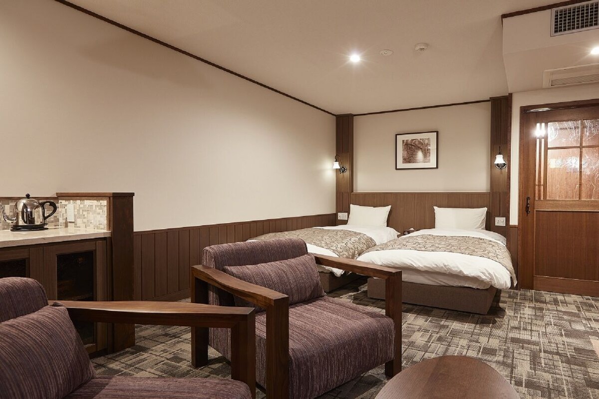 A hotel room with two beds, a wooden desk, and a seating area with chairs.