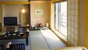 A room with a tatami mat floor, a low table with chairs, a television, and a window with a view. - Hotel Ayase (Rishifuji)