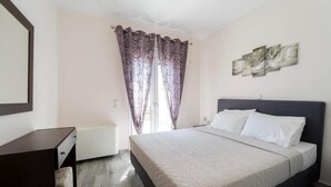 Une chambre à coucher avec un lit, une commode, un radiateur et une fenêtre avec des rideaux.