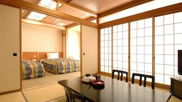 A traditional Japanese-style room with tatami flooring, a low table with chairs, and a sliding door leading to a bedroom.