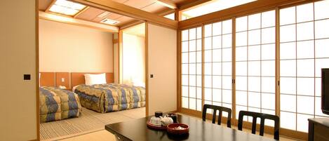 A traditional Japanese-style room with tatami flooring, a low table with chairs, and a sliding door leading to a bedroom.
