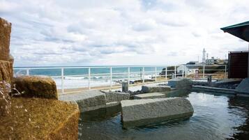 A coastal view with a rocky shoreline, a white railing, and a building with a red roof.