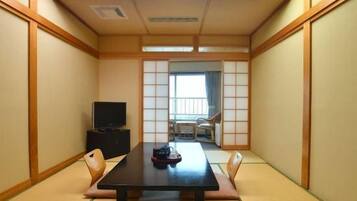 Une pièce de style japonais traditionnel, avec un sol recouvert de tatamis, une table basse, des chaises, un téléviseur et une porte coulissante donnant sur un balcon.