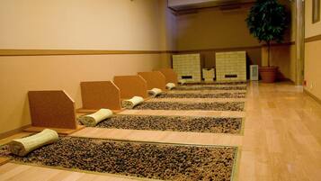 A row of massage chairs with a pebble floor, a potted plant, and a wall-mounted air vent.