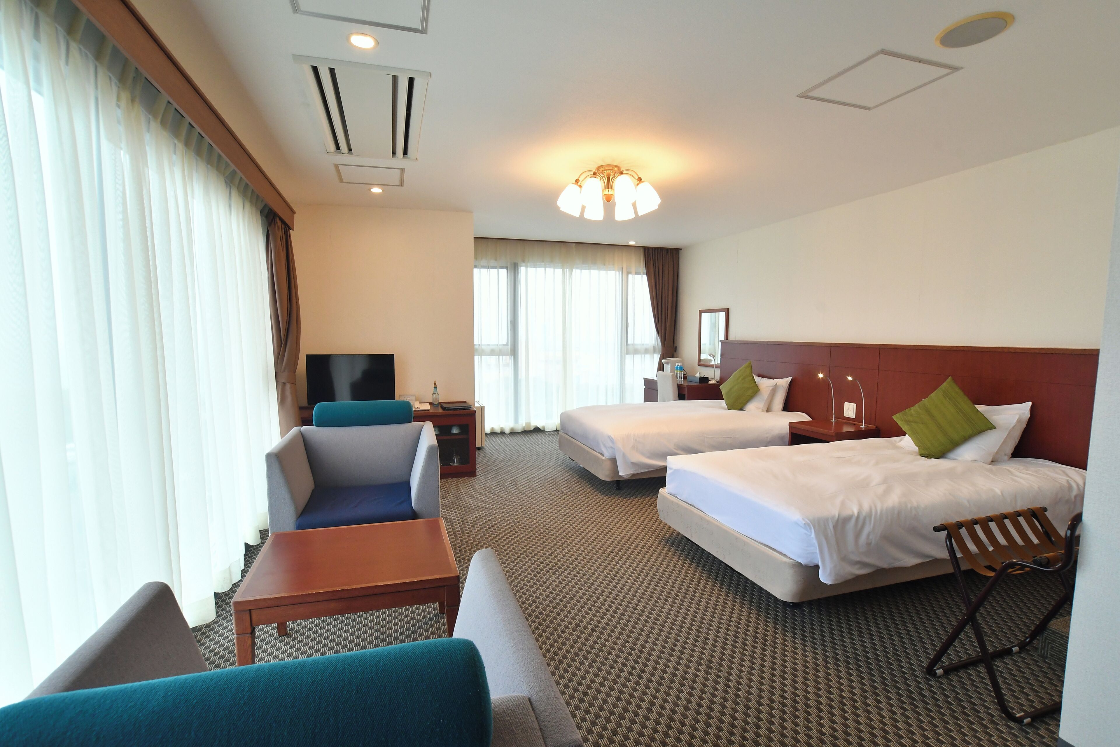A hotel room with two beds, a sofa, a TV, and a desk.