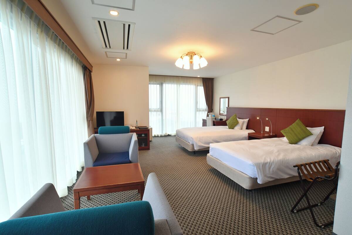 A hotel room with two beds, a sofa, a TV, and a desk.