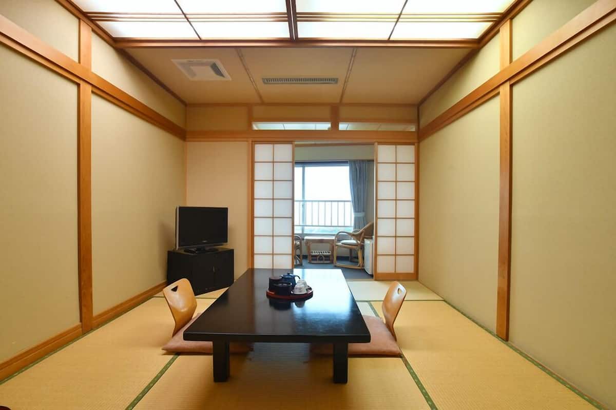 A traditional Japanese room with tatami flooring, a low table, a television, and sliding doors leading to a balcony.