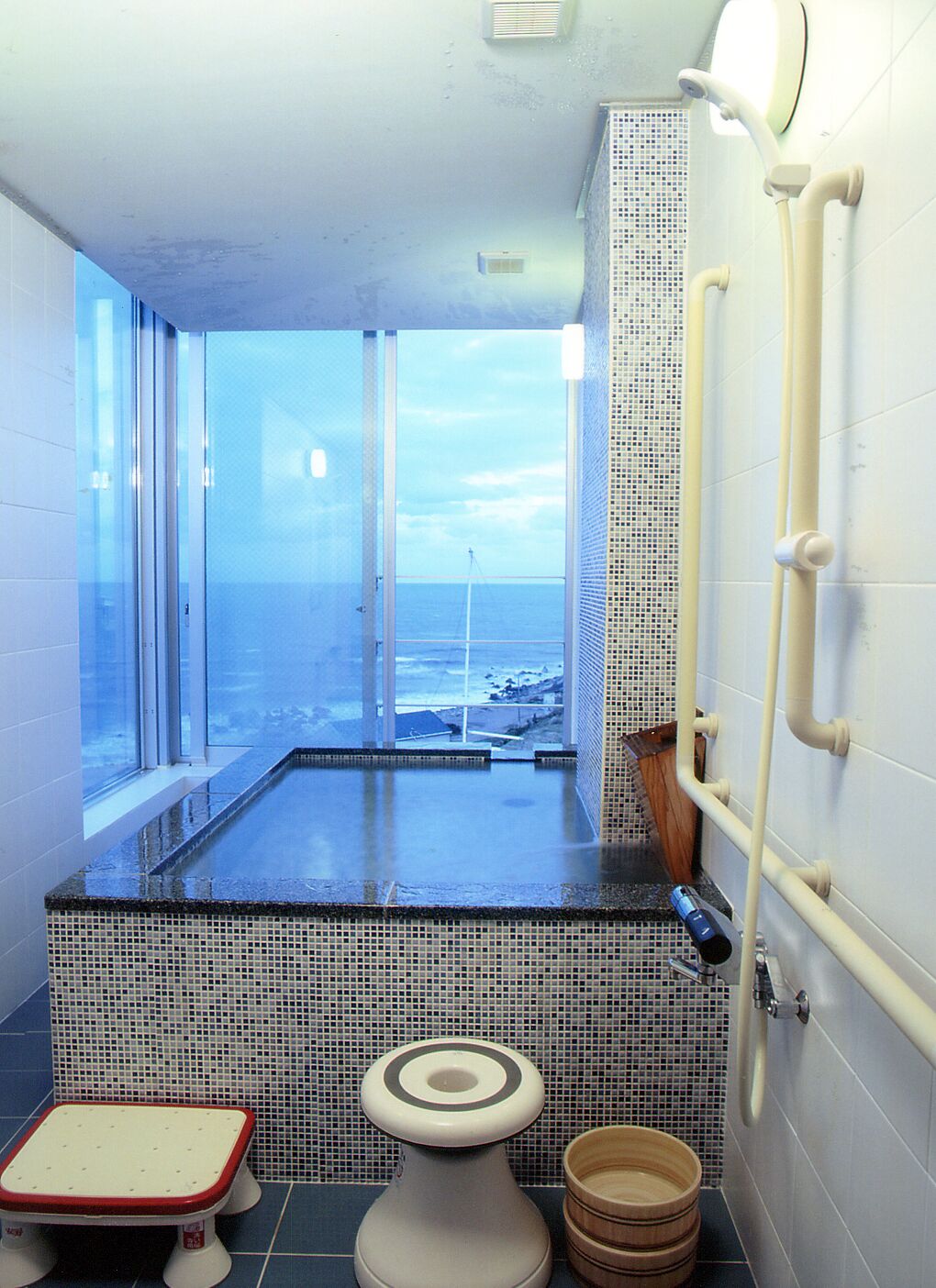 A bathroom with a large window, a bathtub, a toilet, and a shower area.