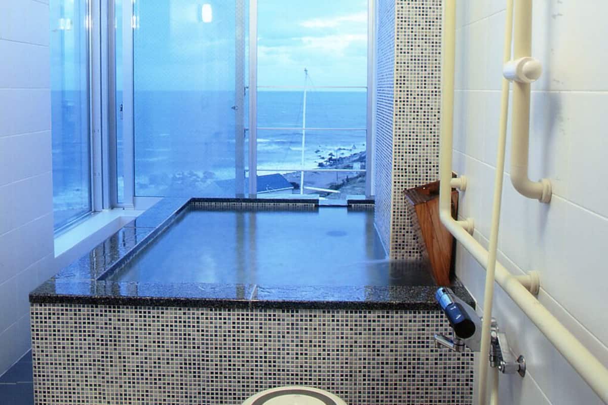 A bathroom with a large window, a bathtub, a toilet, and a shower area.