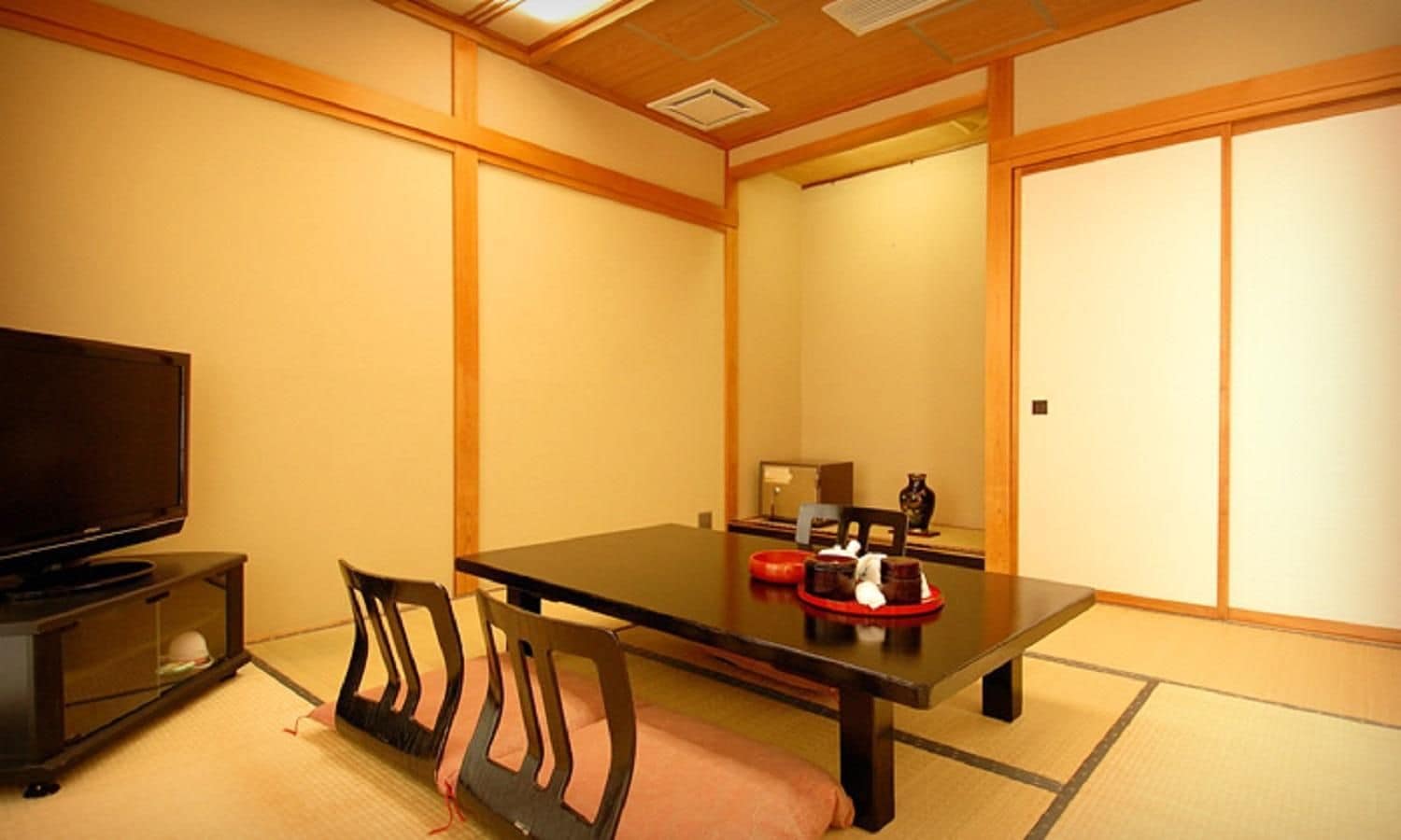 Una habitación de estilo japonés tradicional con suelo de tatami, una mesa baja y un televisor sobre un mueble.