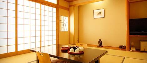 Une pièce de style japonais traditionnel, avec un sol recouvert de tatamis, une petite table avec un coussin, un téléviseur et un vase accroché au mur.