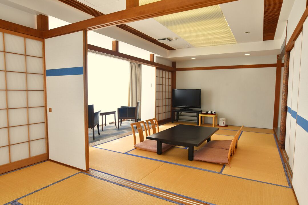 Una habitació japonesa tradicional amb sòls de tatami, una taula baixa, cadires, un televisor i portes corredisses.