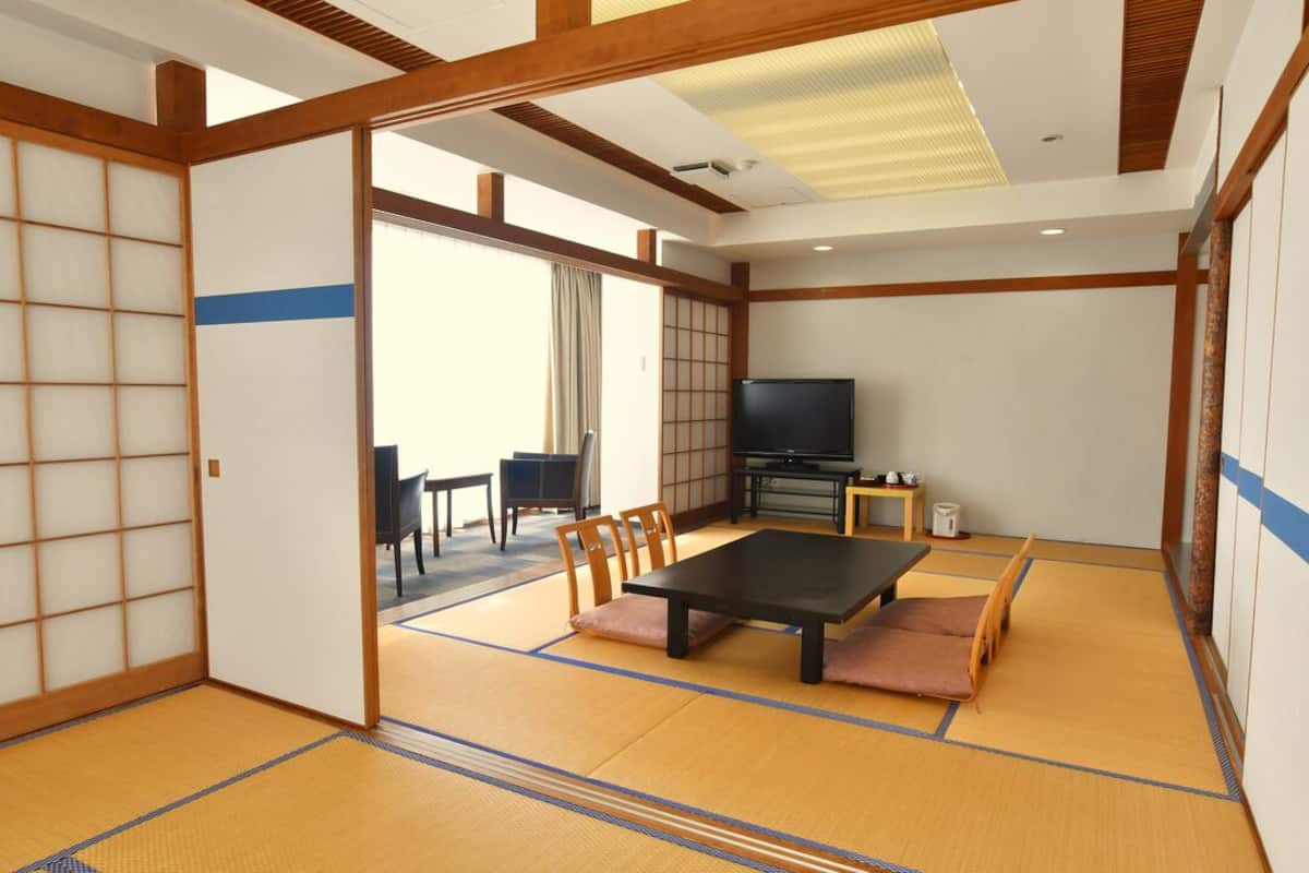 A traditional Japanese room with tatami flooring, a low table, chairs, a television, and sliding doors.