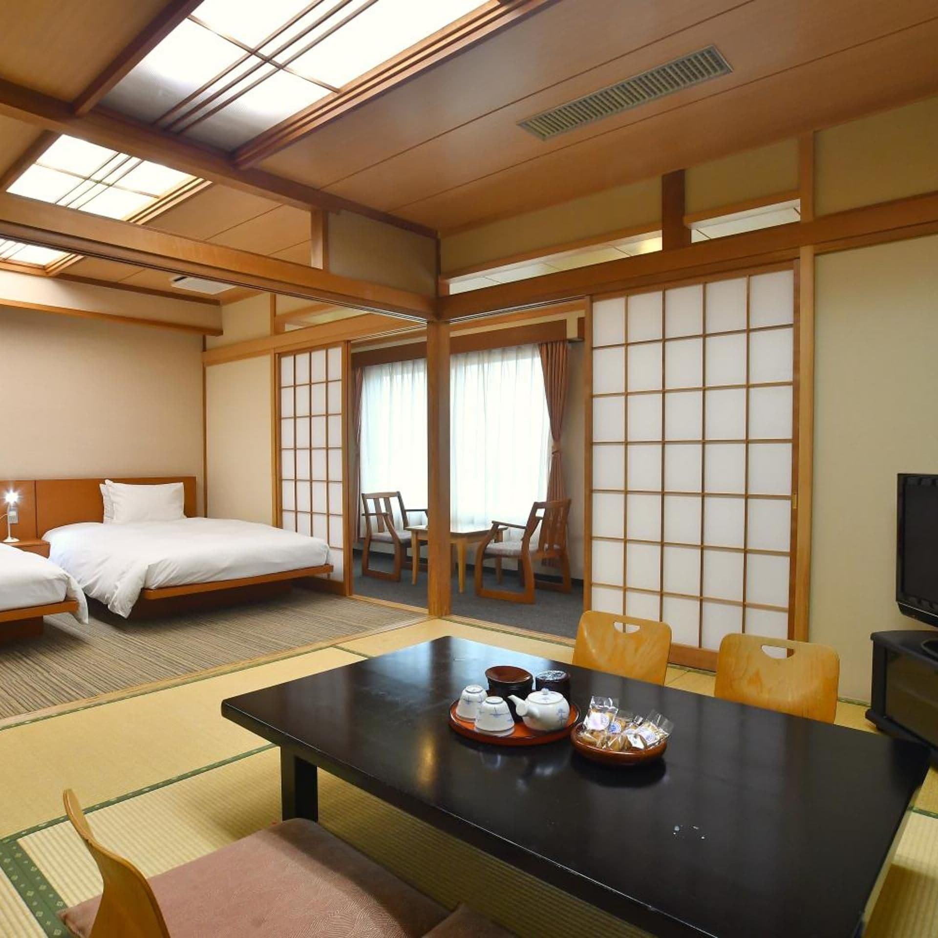 A traditional Japanese-style hotel room with tatami flooring, a low table with tea set, and a bed with white bedding.