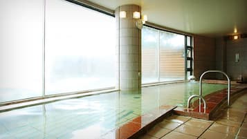 An indoor swimming pool with clear glass walls, a tiled floor, and a metal ladder.